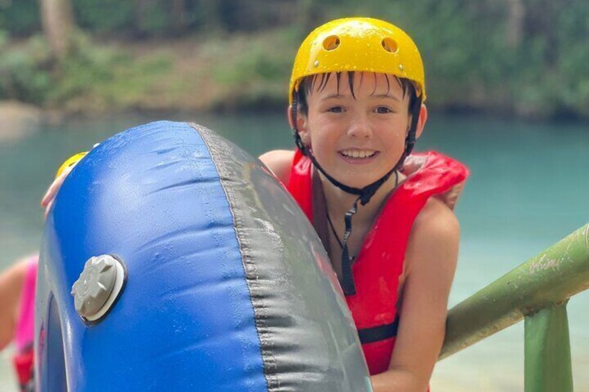 A person wearing a yellow helmet and a red life jacket, leaning on a railing by a body of water. 3