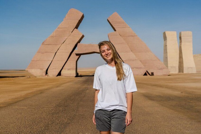 Una persona de pie frente a grandes estructuras de piedra en un paisaje desértico. 4