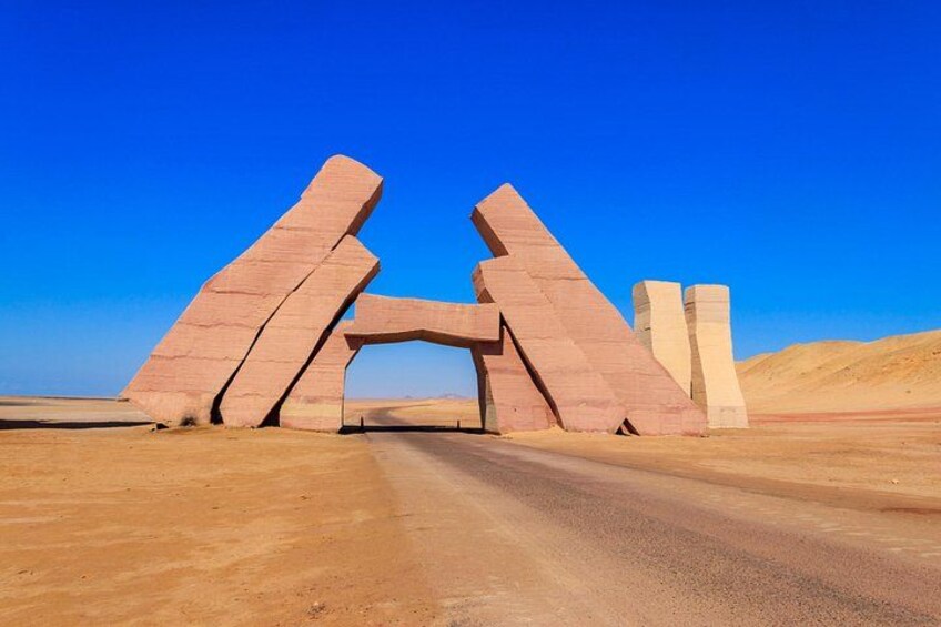 Un paisaje desértico con una gran estructura de piedra en forma de arco, de color rojo. 3