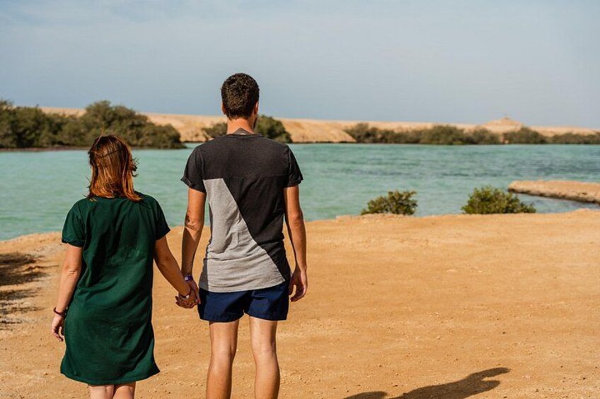 Una pareja caminando por un sendero de tierra junto a un cuerpo de agua, con colinas al fondo. 5