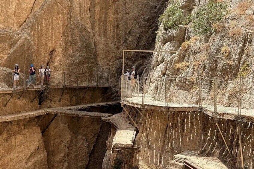 Un puente de madera estrecho sobre un cañón, con personas caminando. 2
