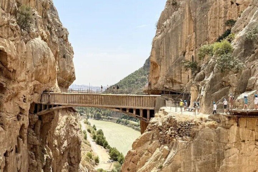 A wooden bridge over a canyon with a river below and a hilly landscape in the distance. 1