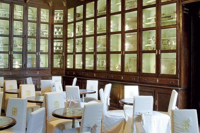 A room with round tables and chairs, large wooden cabinets with glass doors, and a chandelier. 3