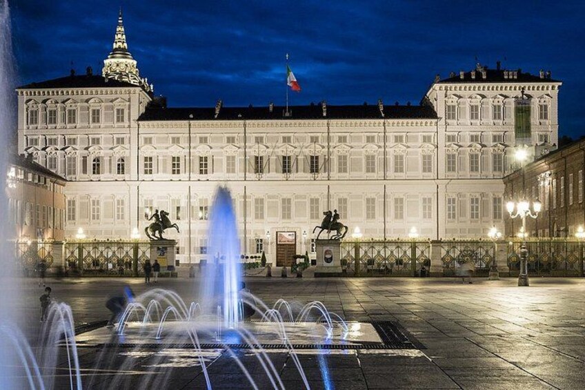 A large white building with a fountain in front, a statue, and a flag. 1