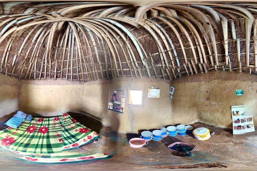 A traditional hut with a thatched roof, a woven mat on the floor, and several bowls and plates on the wall. 2