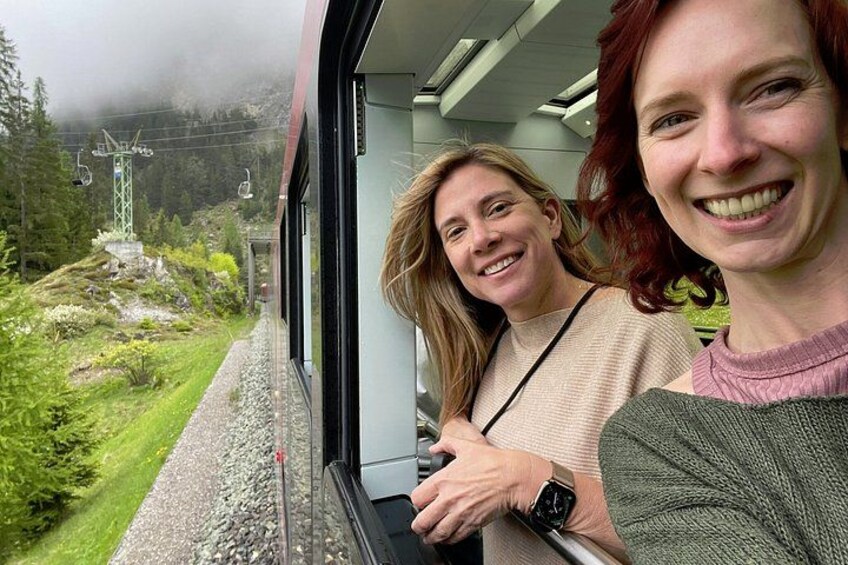 Two people on a train with a view of a mountainous landscape and power lines. 3