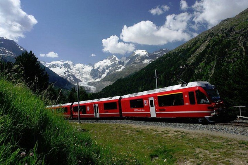 A red train on tracks with snow-capped mountains in the background. 2