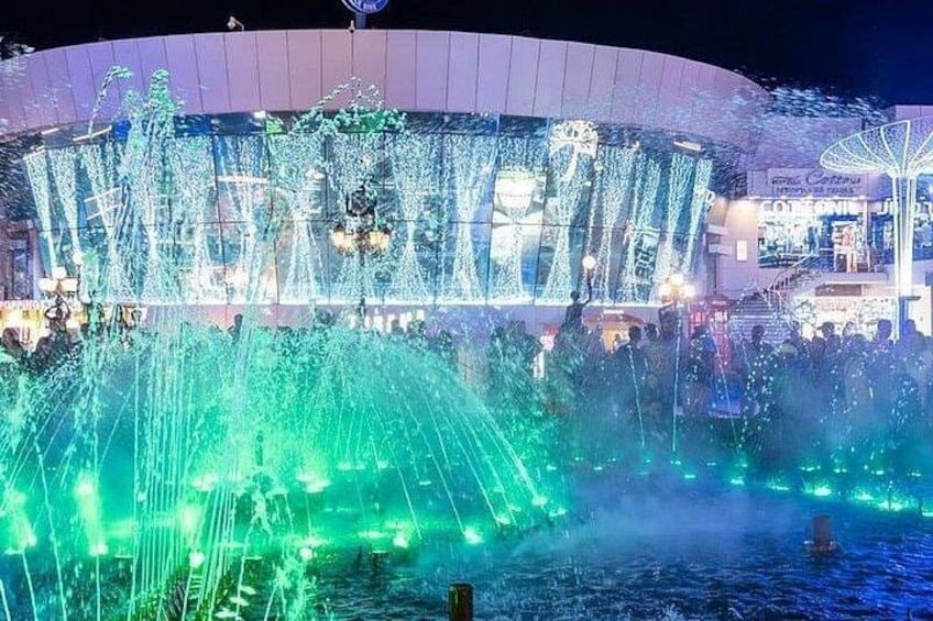 A water fountain with lights, a building in the background, and a sign. 3