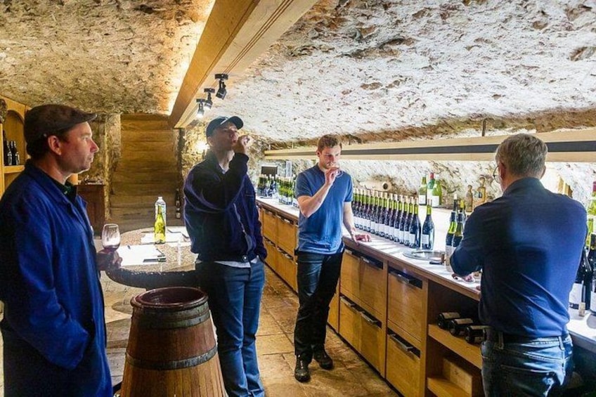 A group of people in a rustic cellar with wooden barrels and bottles of wine. 4