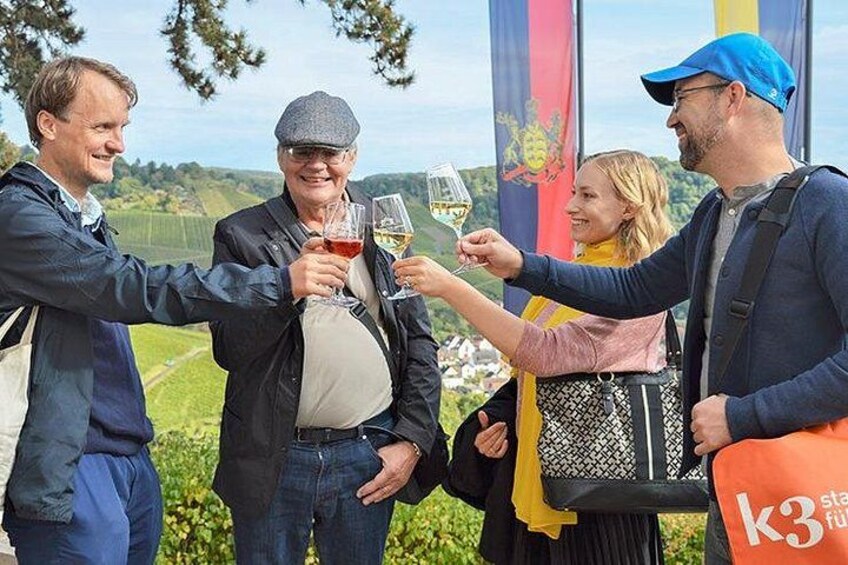 A group of people toasting with wine glasses in an outdoor setting with greenery and flags in the background. 1