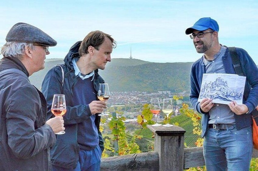 Three people standing outdoors, holding wine glasses, with a vineyard and a hill in the background. 2