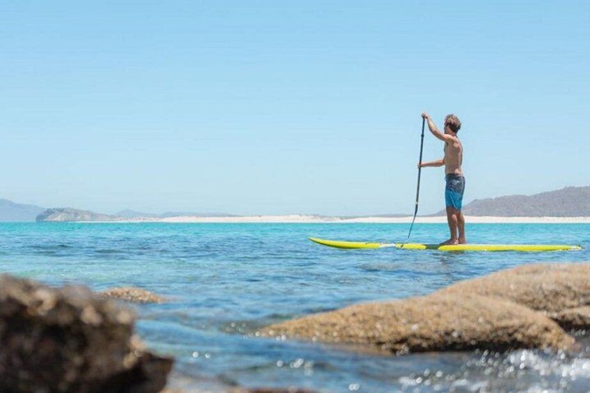 A person paddleboarding on a calm sea with clear skies and distant land. 2