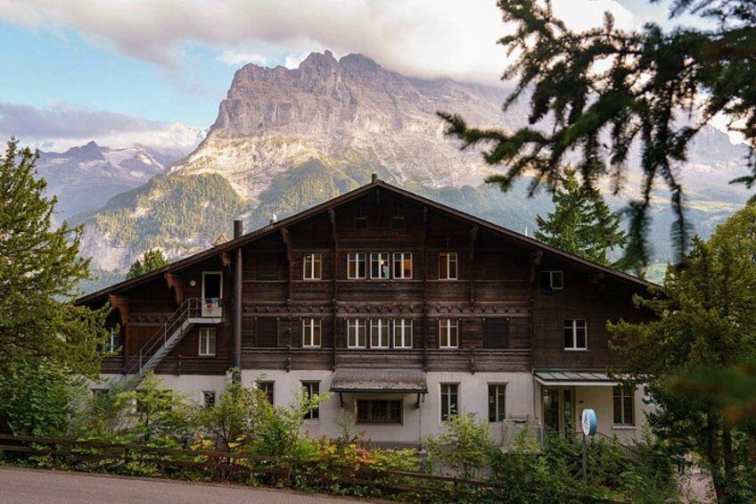 A wooden chalet with a balcony, surrounded by trees and mountains in the background. 4