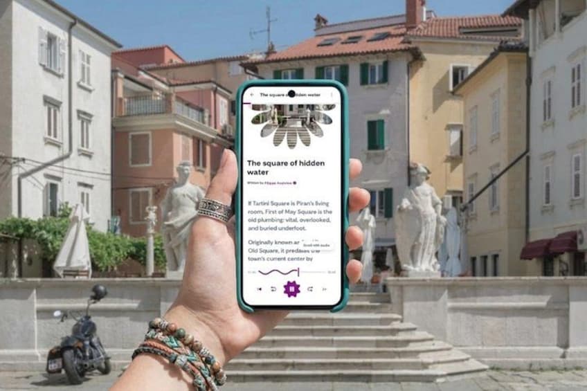 A hand holding a smartphone displaying an article titled 'The square of hidden water' with a background of a historic square with statues and buildings. 1