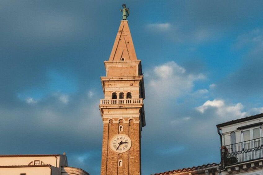 A tall brick tower with a clock and a statue on top, under a cloudy sky. 5