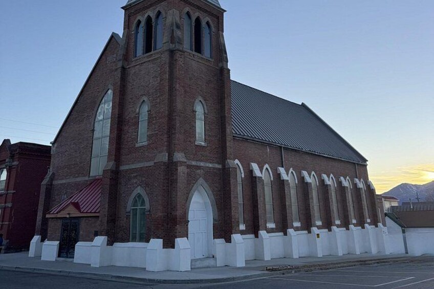 A brick church with a steeple, large arched windows, and a white fence in front. 4