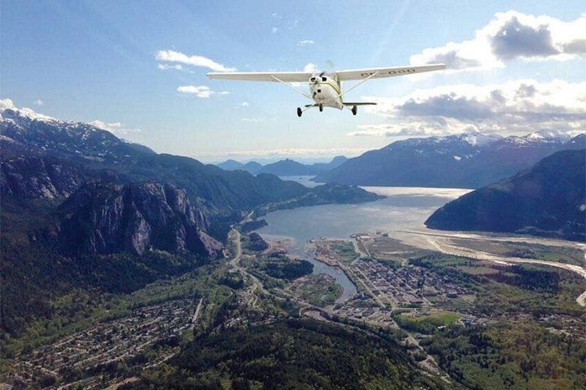 Un petit avion survole un paysage montagneux, avec une rivière et une ville en contrebas. 1