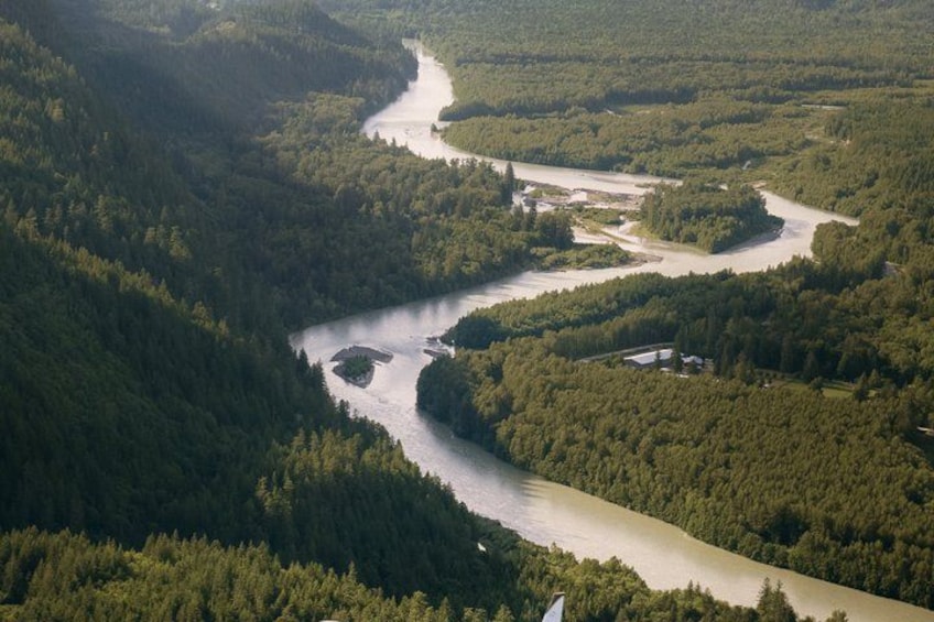 A river winding through a densely forested valley with a small settlement near the riverbank. 2