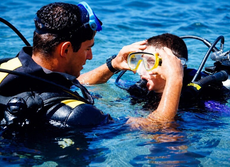 Two scuba divers in clear water, one assisting the other with their equipment. 2
