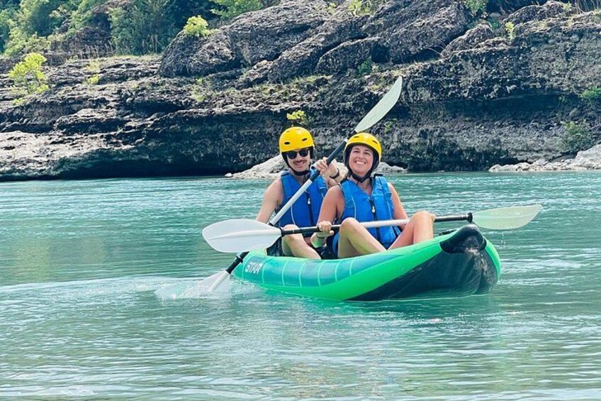 Two people kayaking on a river with rocky banks. 1