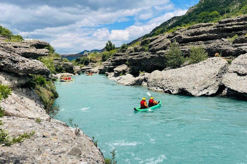 A river with kayaks, rocky banks, and greenery. 2