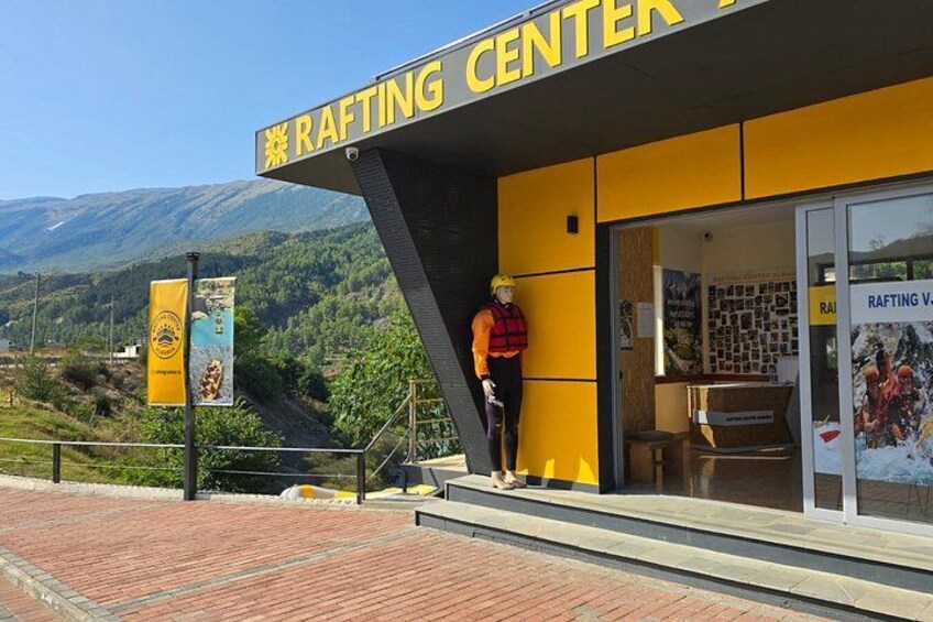 A rafting center with a yellow exterior, a mannequin in a life jacket, and a mountainous landscape in the background. 3