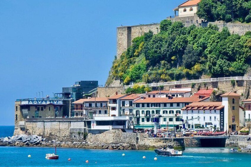 A coastal town with historic buildings, a castle on a hill, and boats in the water. 2