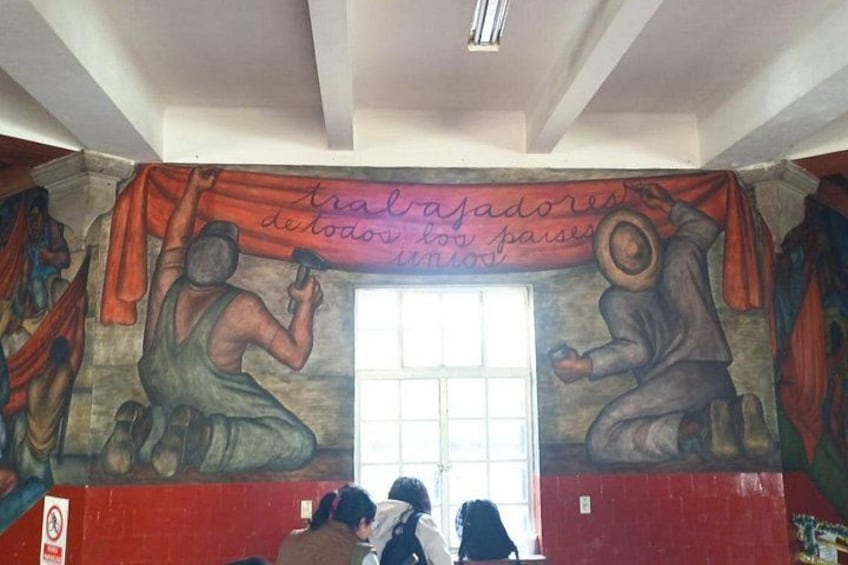 Un mural con figuras y texto, una ventana y una pared roja. 1