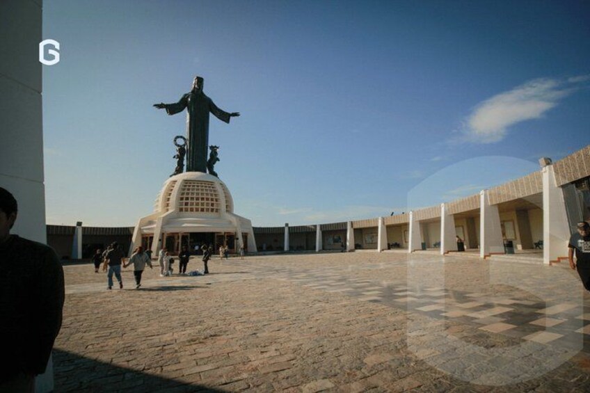 A plaza with a statue, people walking, and a building with columns. 2