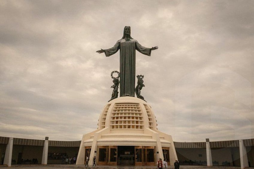 A large statue with outstretched arms, a base with a grid pattern, and two smaller statues on either side. 3
