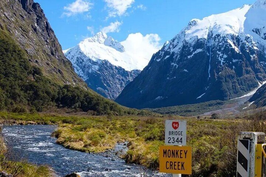 A river, a sign for Monkey Creek Bridge, and snow-capped mountains in the background. 5