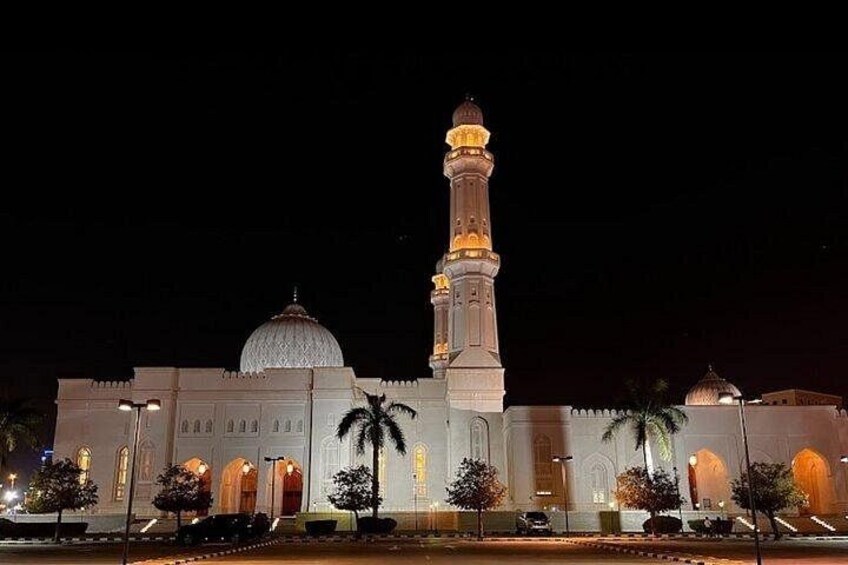 A mosque with a large dome and a tall minaret, illuminated at night. 4