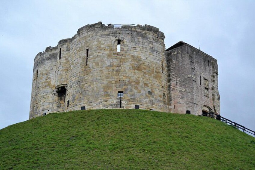 A large, circular stone castle on a grassy hill. 5