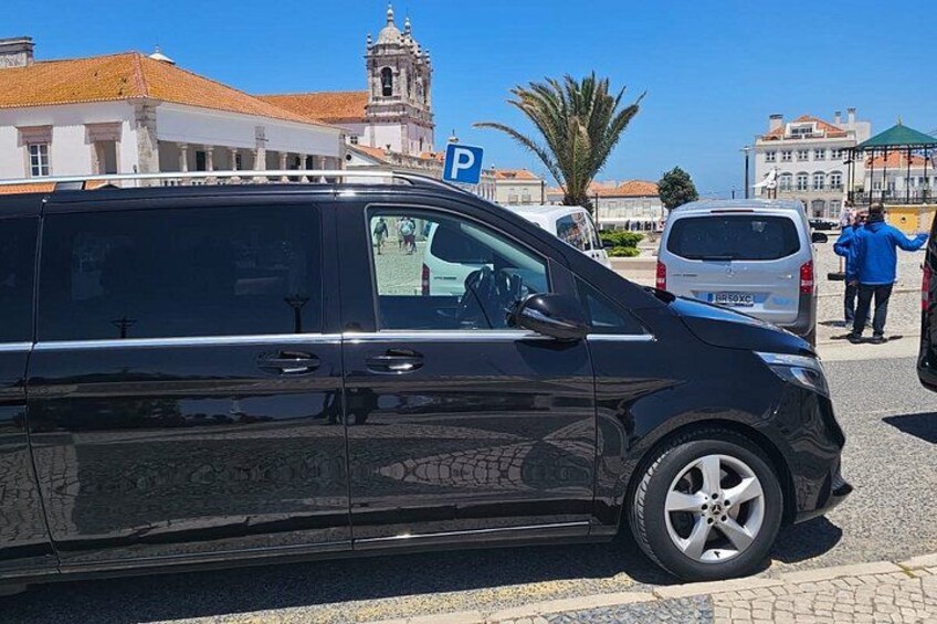 A black van parked on a street with a 'P' parking sign, buildings, and a tower in the background. 4