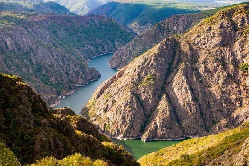A canyon with a river, steep cliffs, and sparse vegetation. 2