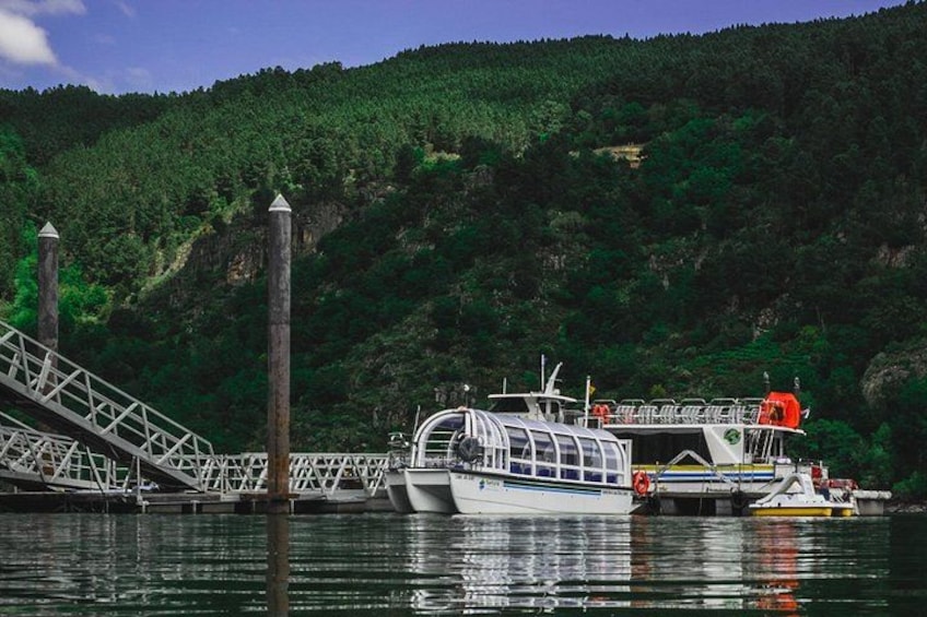 A boat docked at a pier with a forested hillside in the background. 3