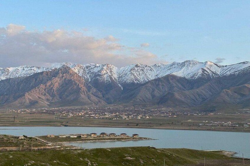 A mountainous landscape with snow-capped peaks, a body of water, and a small settlement. 1