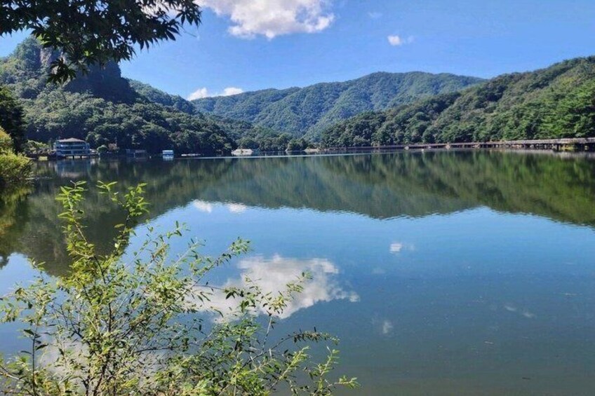 A calm lake with reflections of trees and mountains, a bridge, and a boat. 4