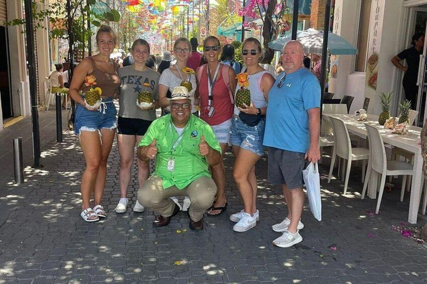 Un grupo de personas posando en una calle empedrada con mesas al aire libre y decoración tropical. 5