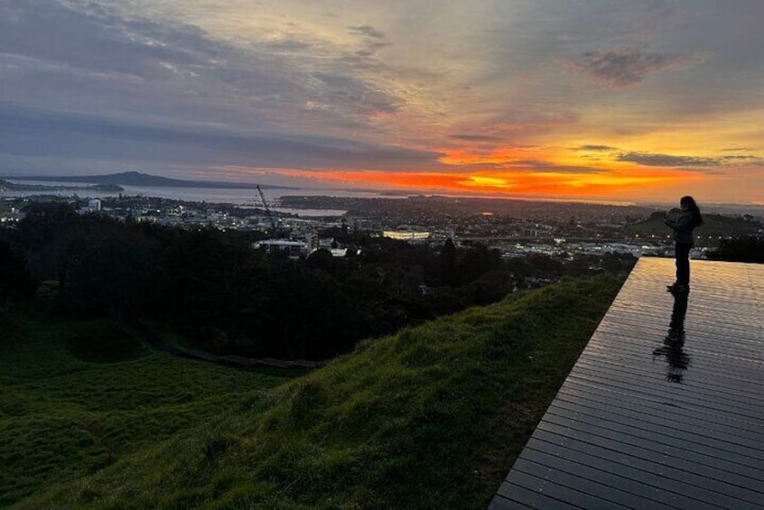 A person standing on a wooden deck overlooking a cityscape during sunset. 1