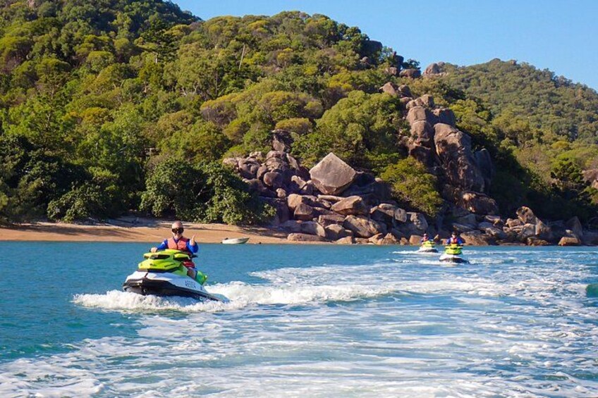 To jetski på rolige bølger med en klippefyldt kystlinje og frodig, grøn vegetation i baggrunden. 4