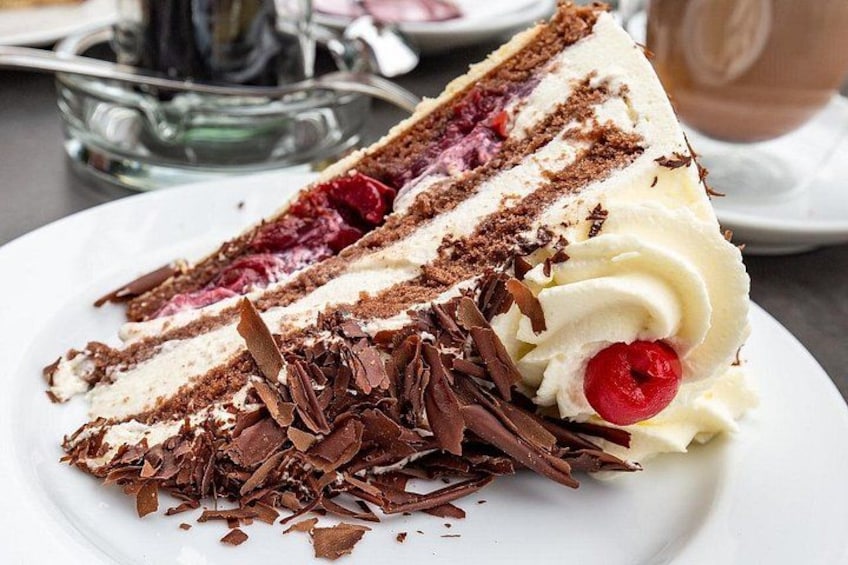 A slice of layered cake with whipped cream and chocolate shavings on a plate. 1