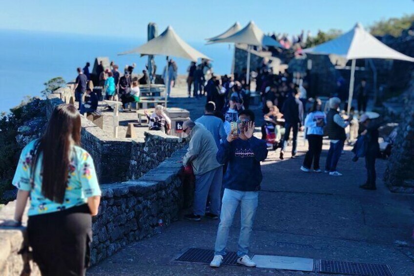 A crowded coastal walkway with people walking and taking photos. 3