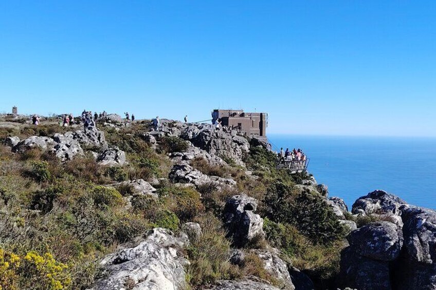 A rocky coastal landscape with a historic building and a viewing platform overlooking the sea. 4