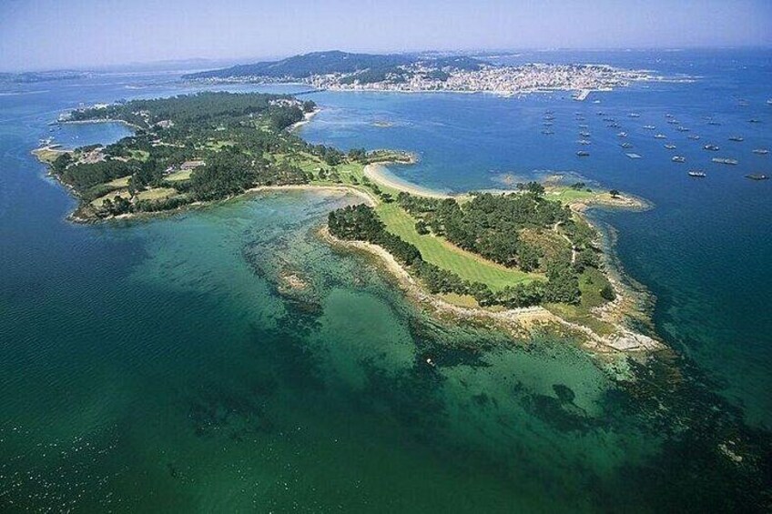An aerial view of a coastal area with a large island surrounded by clear blue waters, a small peninsula, and a distant city skyline. 5