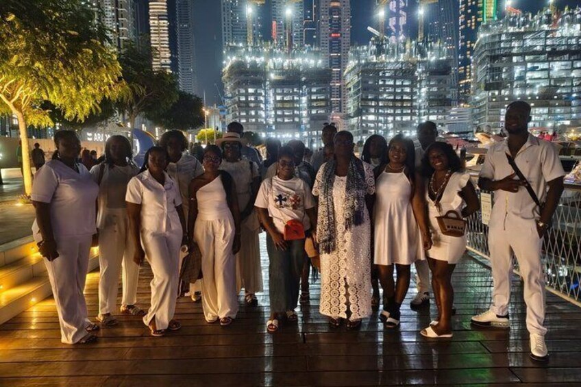 A group of people in white attire standing on a waterfront promenade with a city skyline in the background. 5