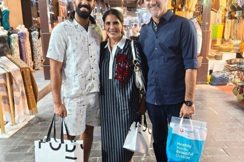 Three people standing in a market with patterned textiles and bags. 3