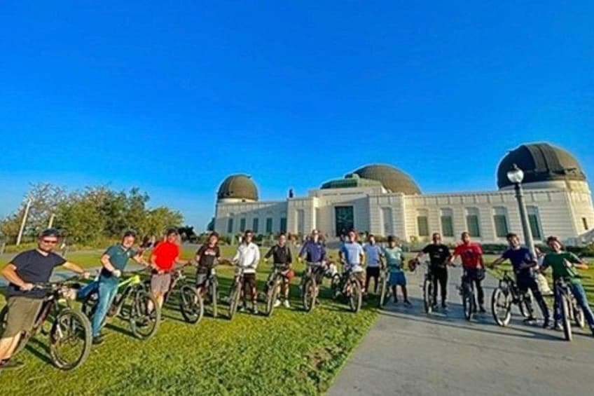 Un grupo de personas en bicicletas frente a un edificio con dos cúpulas. 1