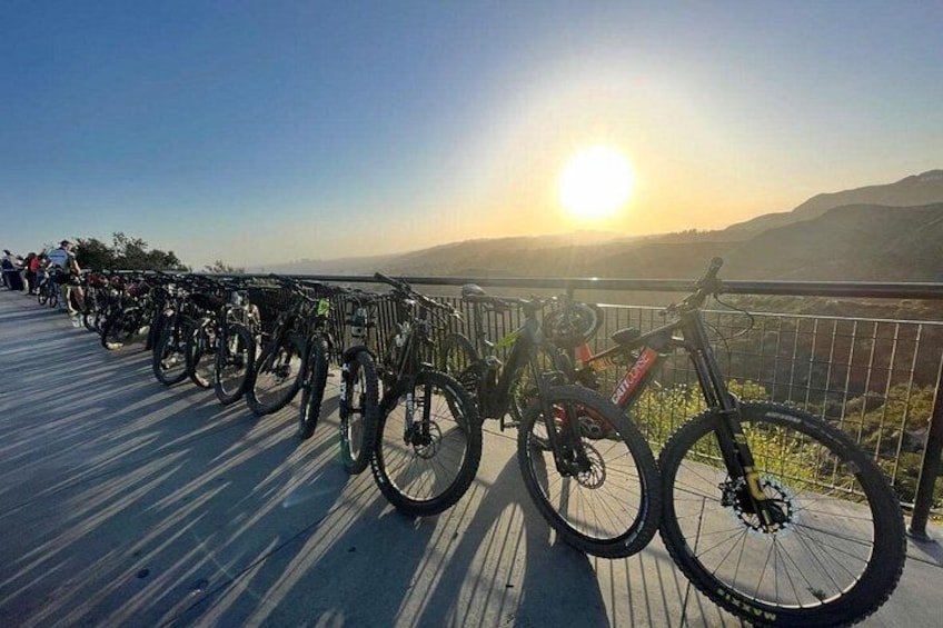 Varias bicicletas están estacionadas en una cubierta de madera con un atardecer al fondo. 3