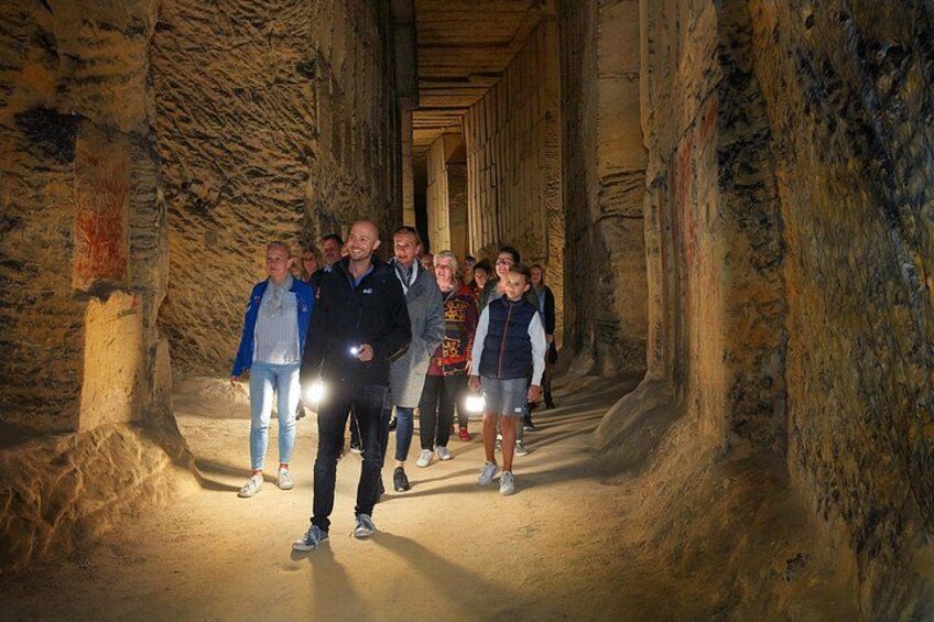 A group of people walking through a narrow, dimly lit passage with stone walls. 3